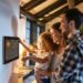 In this warm and inviting scene, we see a young family bonding over advanced technology as they interact with a smart home device. A mother, father, and their child are gathered in a cozy, well-lit room, with smiles on their faces, clearly enjoying the ease and convenience of controlling their home environment with just a few taps. The smart home system appears user-friendly, drawing the family closer through shared moments of modern living.